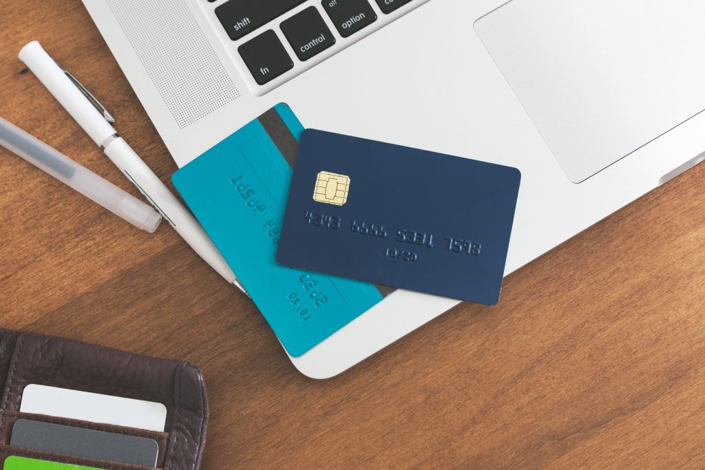 Photograph of credit cards placed on a laptop, alongside some pens and a wallet.