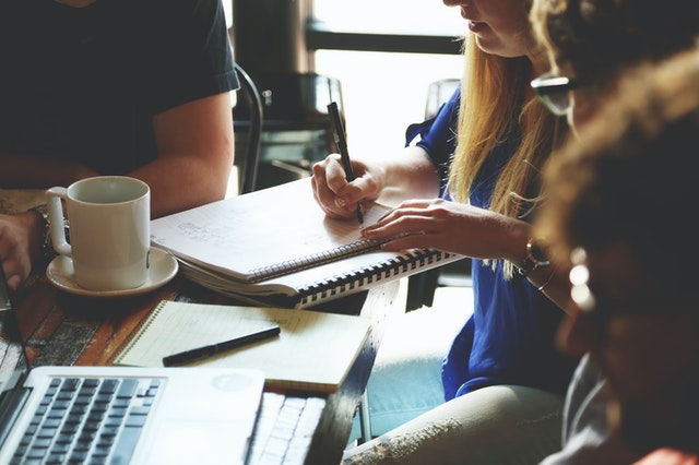 Group of university students studying together around a table in a coffee shop .