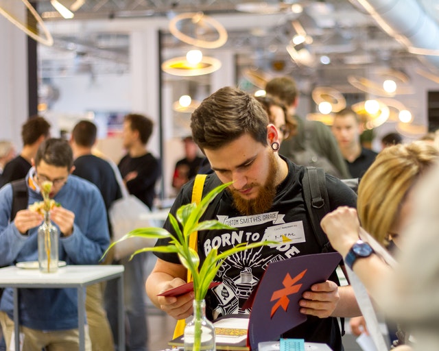 Young man looking at a book in a busy room full of students at a university careers event