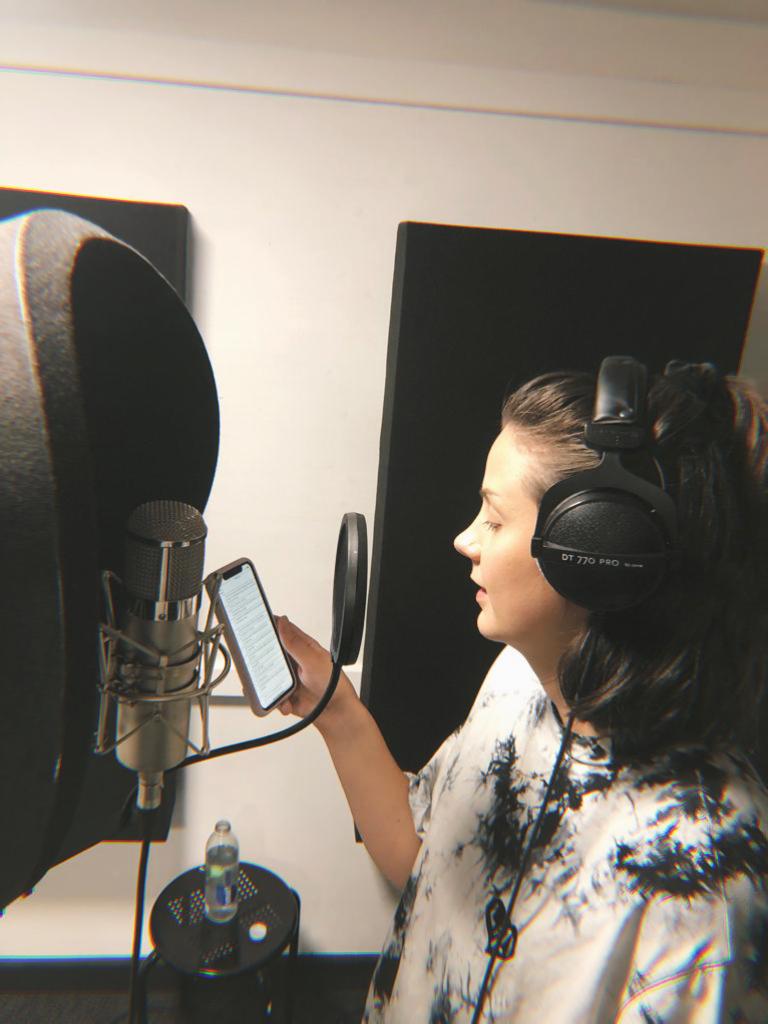 Female voiceover artist with headphones on, reading a script at a microphone in a music studio