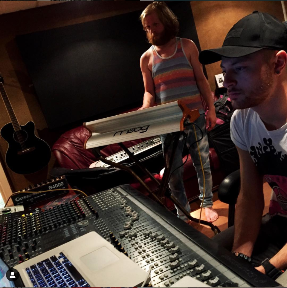 A male musician stands at his synthesiser as a studio technician sits at the mixing desk.