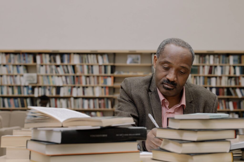 Academic sitting next to piles of books, taking notes