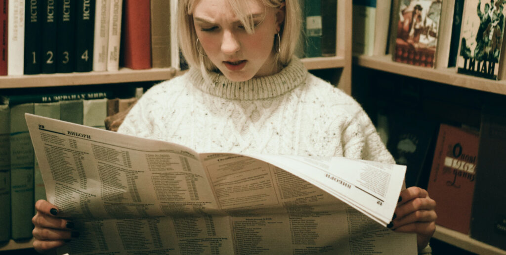 Young blonde woman reading a newspaper